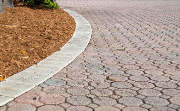 Child's eye view of octagon and square shaped brick pavers with curved section of driveway with rectangle bricks along edge showing plant and mulch pile. Curves to left.