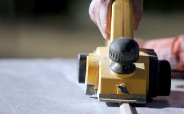 Close-up of a construction worker's hand and power tool while planing a piece of wood trim for a project (shallow focus).