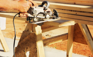 Carpenter uses worm-drive circular saw to cut lumber plank at construction work site.  Sedona, Arizona, 2010.