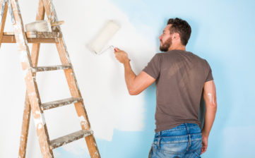 Portrait of handsome young painter in paint splattered shirt painting a wall with paint roller