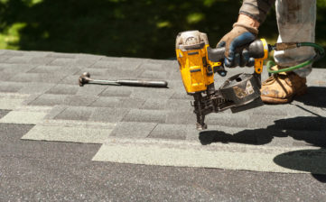 Roofers replacing old roof shingles with New shingles on residential home using a nail gun.