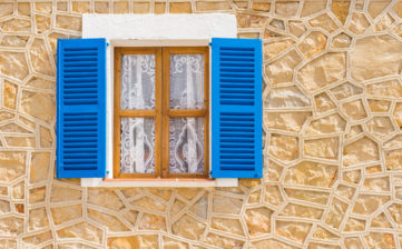 Detail view of blue open wooden window shutters and rustic wall of mediterranean house