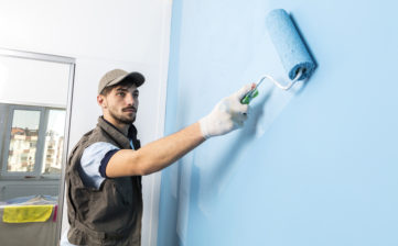 Young man painting a wall blue with a roller